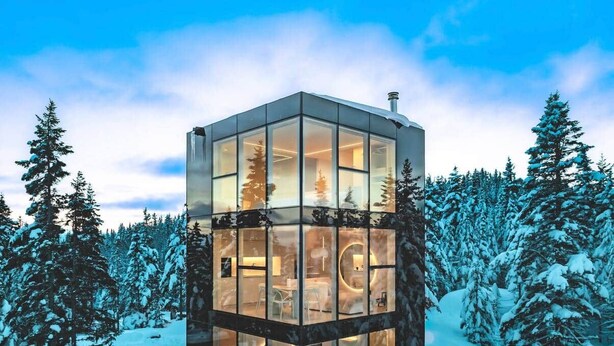 Een modern, kubusvormig glazen gebouw, omringd door met sneeuw bedekte bomen.