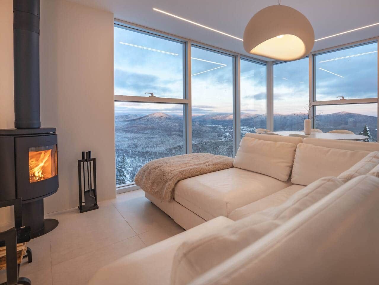 A modern interior with a sofa, a fireplace, and large windows offering a view of a snowy landscape.