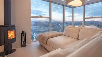 A modern interior with a sofa, a fireplace, and large windows offering a view of a snowy landscape.