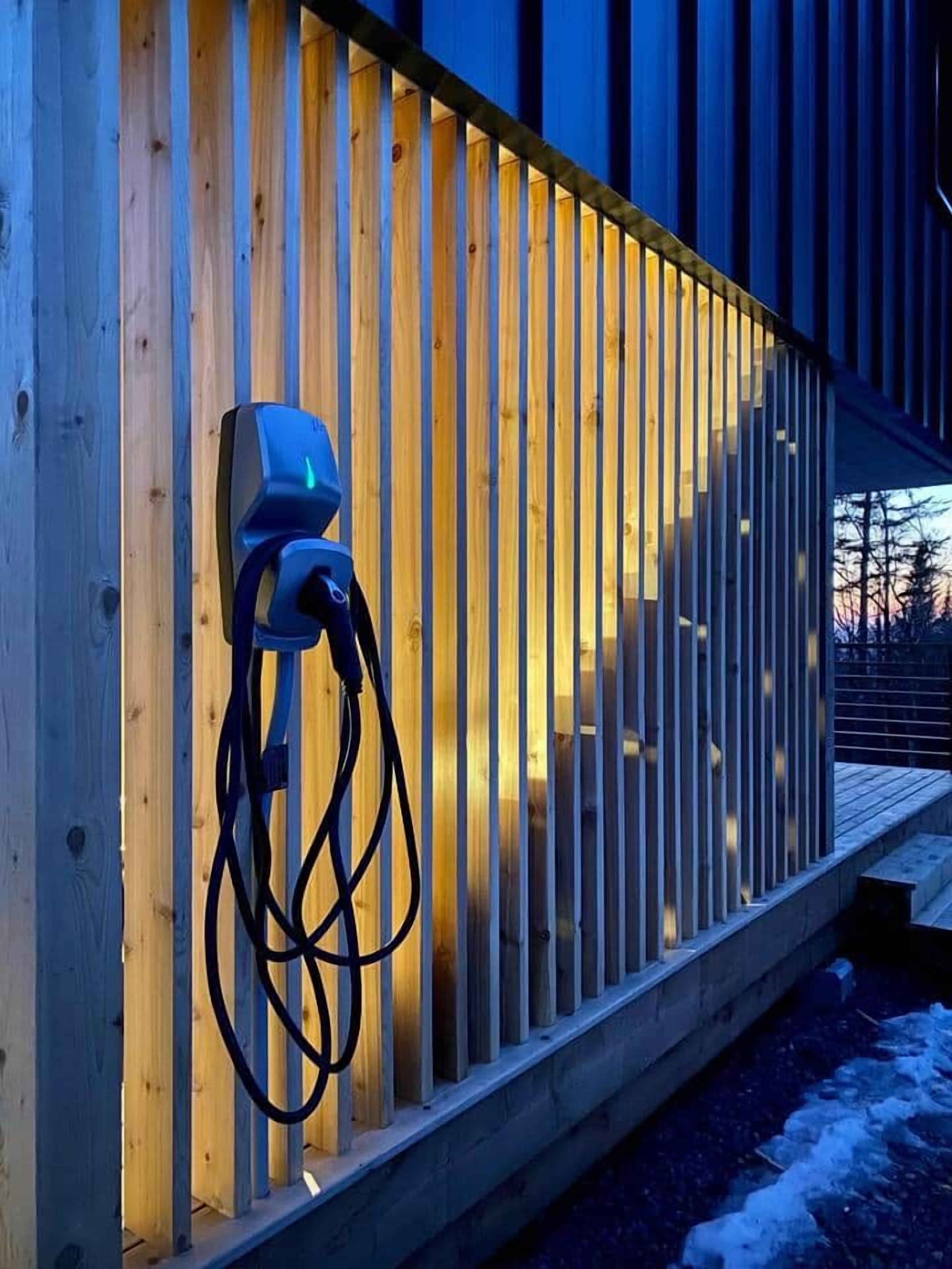 An electric vehicle charging station mounted on a wooden fence.
