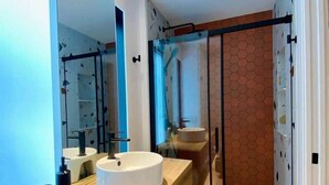 Un bagno moderno con un lavabo rotondo, uno specchio e una cabina doccia in vetro.