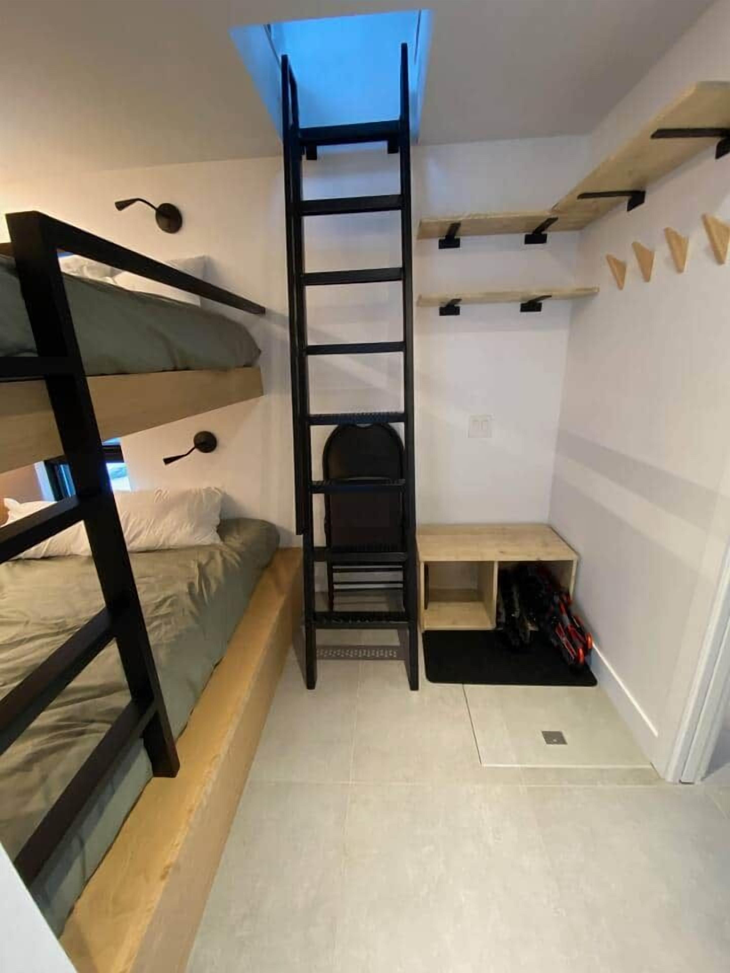 Habitación pequeña con una cama individual superpuesta, una escalera, un escritorio y una estantería.