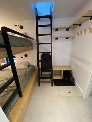 Habitación pequeña con una cama individual superpuesta, una escalera, un escritorio y una estantería.