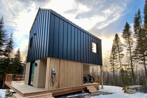 A modern cabin with a sloped roof, wooden deck, and a bicycle parked outside. - MIST / Micro-Chalet / Nature Immersion (Capitale-Nationale)
