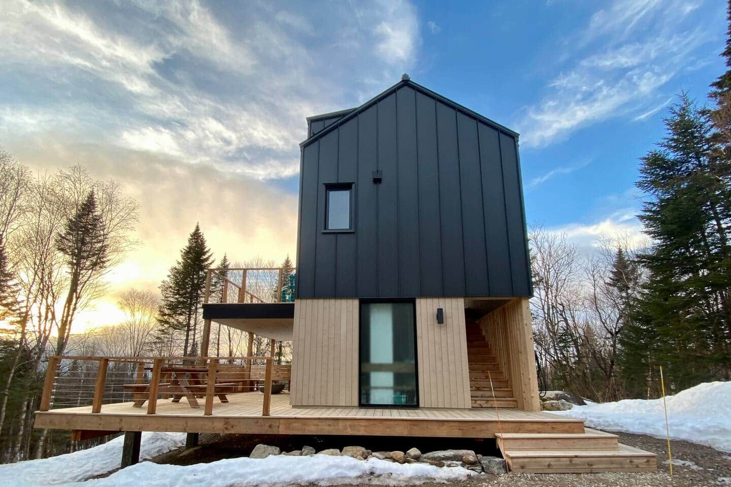En modern stuga med mörk exteriör, en träveranda och en entré med glasdörr.