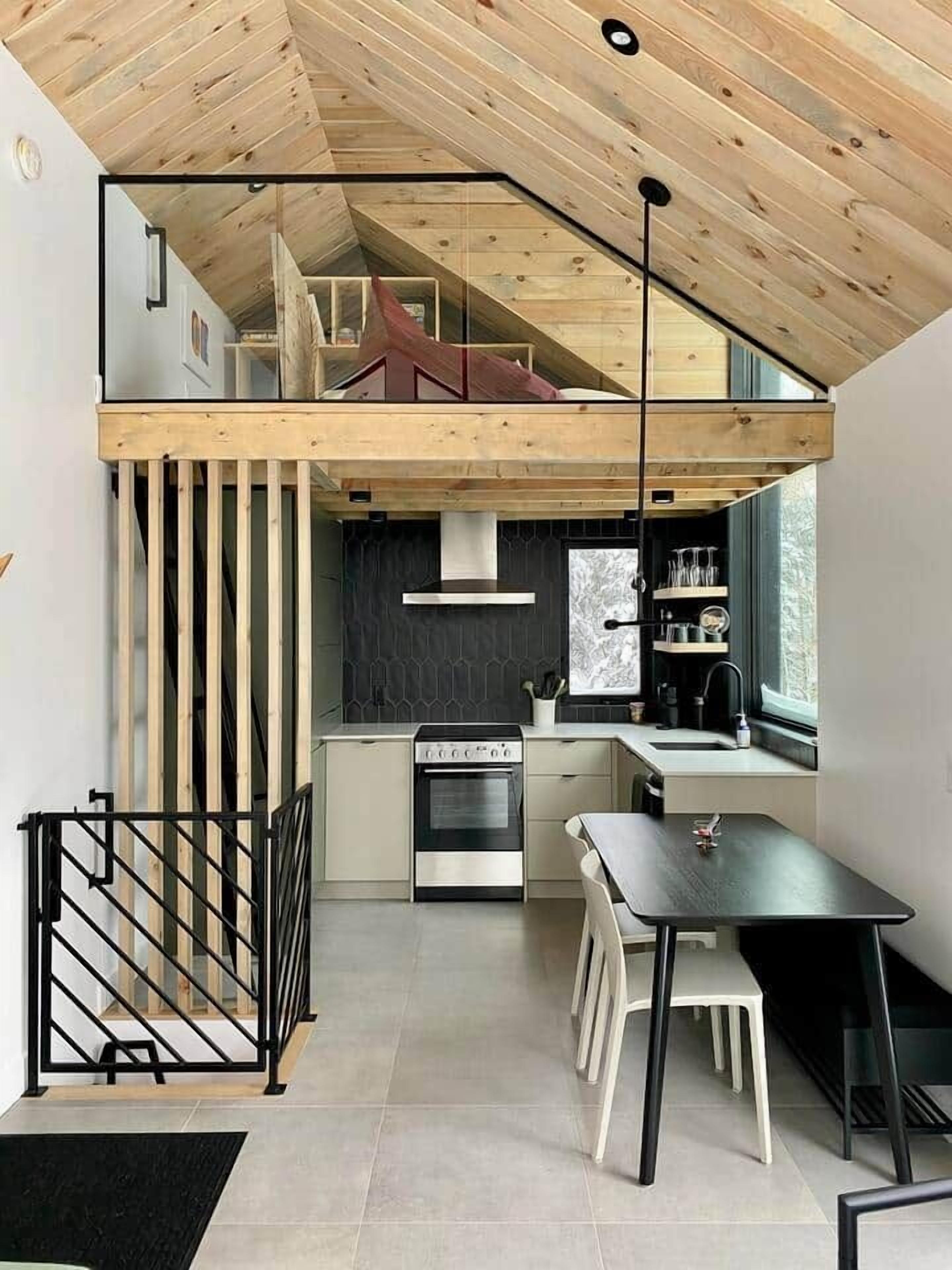 Une cuisine compacte au design moderne, dotée d’un four encastré, d’un coin repas avec une table et des chaises, et d’un espace en mezzanine situé au-dessus.
