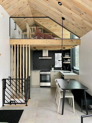 Cocina compacta de diseño moderno, con horno empotrado, zona de comedor con mesa y sillas, y un altillo superior.