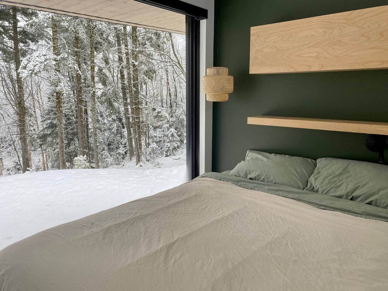 Une chambre avec une grande fenêtre, un lit et une étagère fixée au mur.
