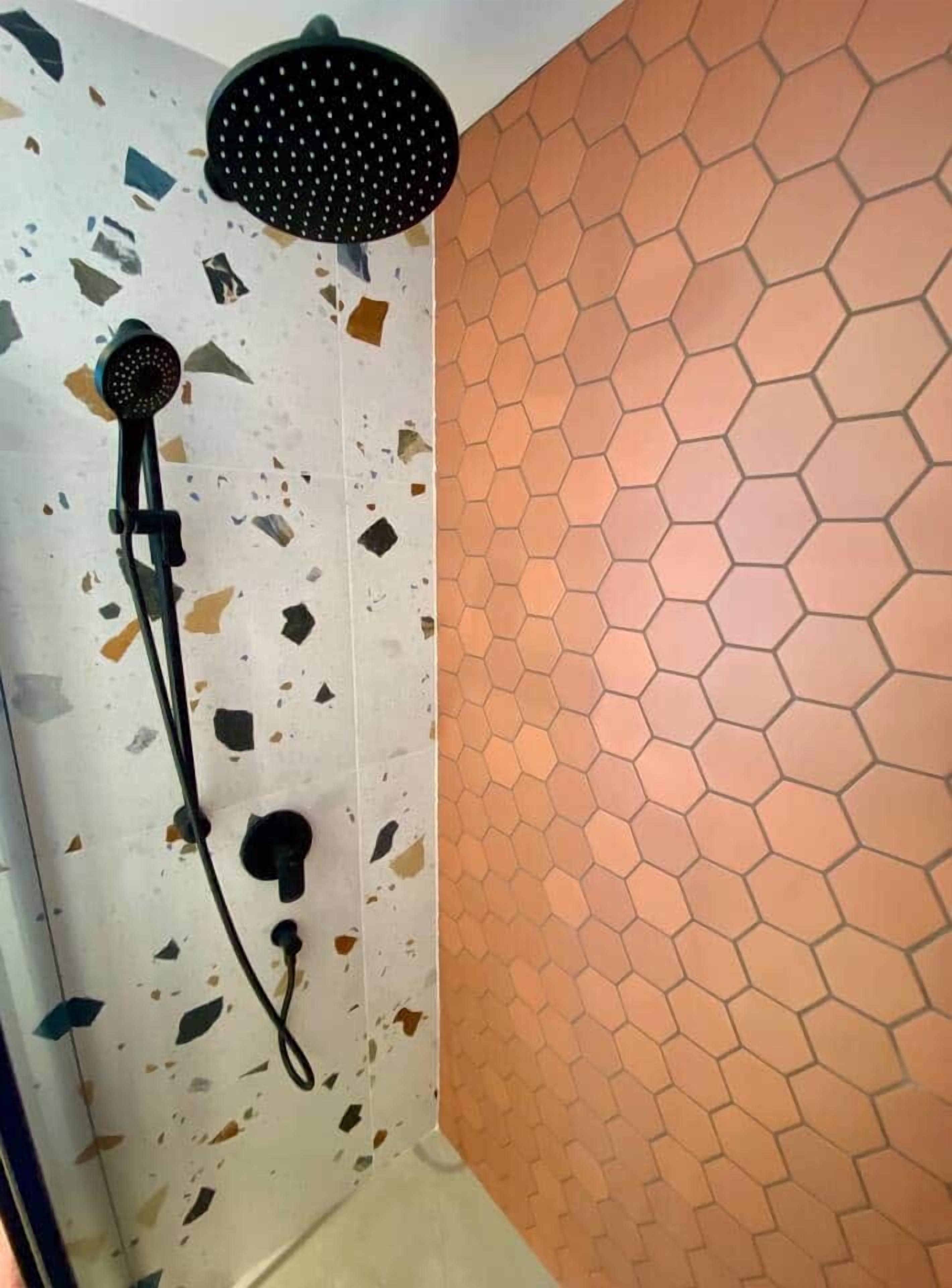 A shower with a handheld showerhead and a wall with a hexagonal tile pattern.