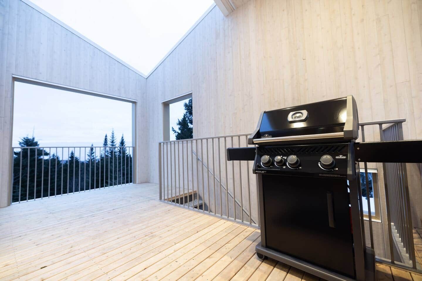 A modern outdoor kitchen with a grill, a wooden deck, and a view of trees.