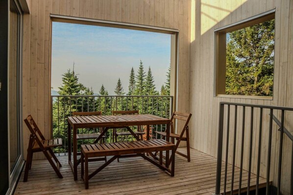 A wooden deck with a table and chairs, overlooking a forested area.