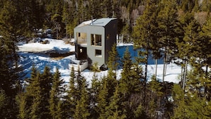 Une cabane moderne dotée d’un toit plat, entourée d’une forêt et de neige.