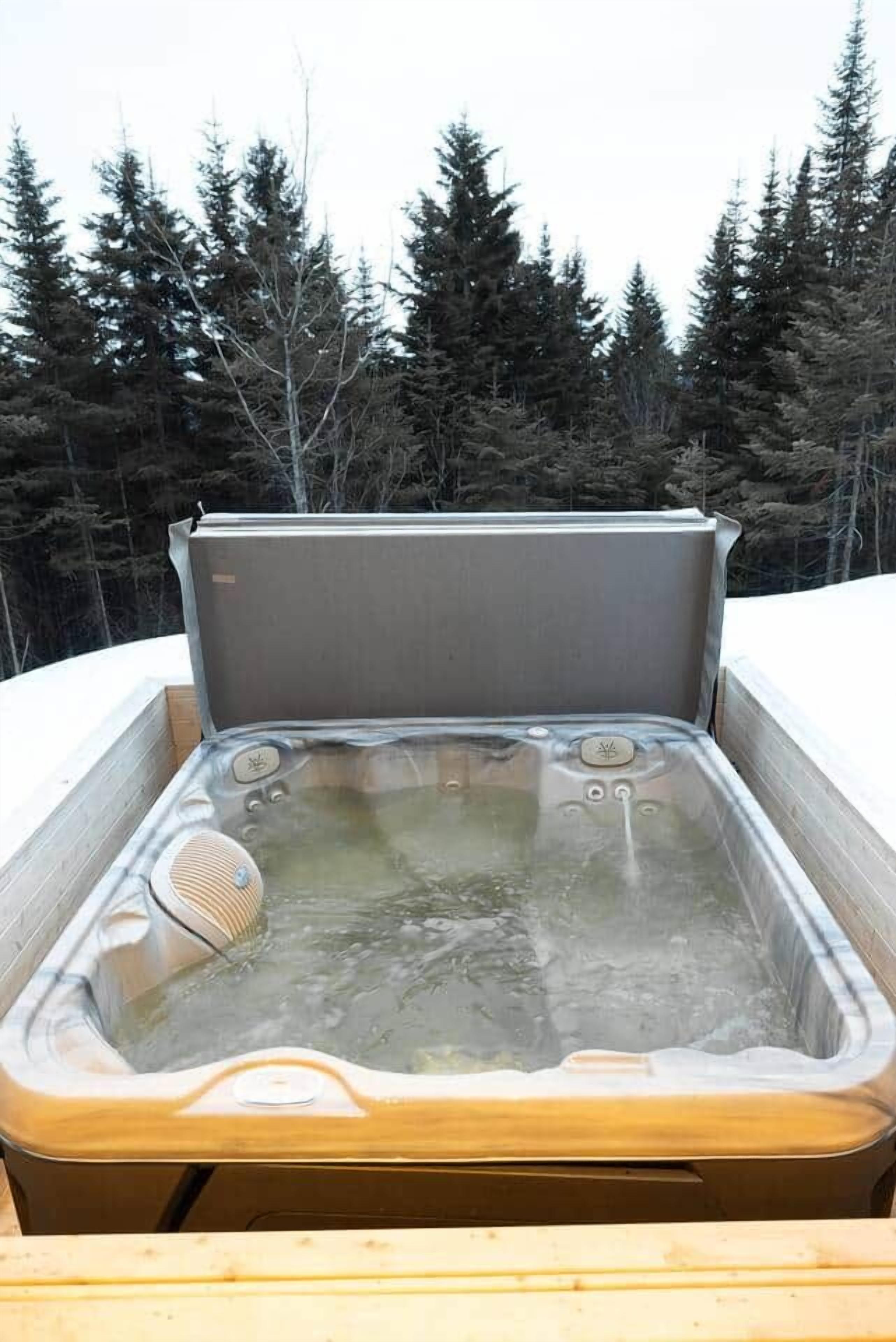A hot tub with a wooden deck, surrounded by a forest.