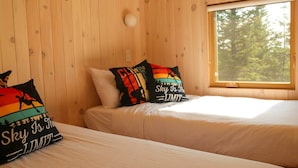 Une chambre avec deux lits, des murs en bois, une fenêtre donnant sur la forêt et des oreillers ornés de messages inspirants.