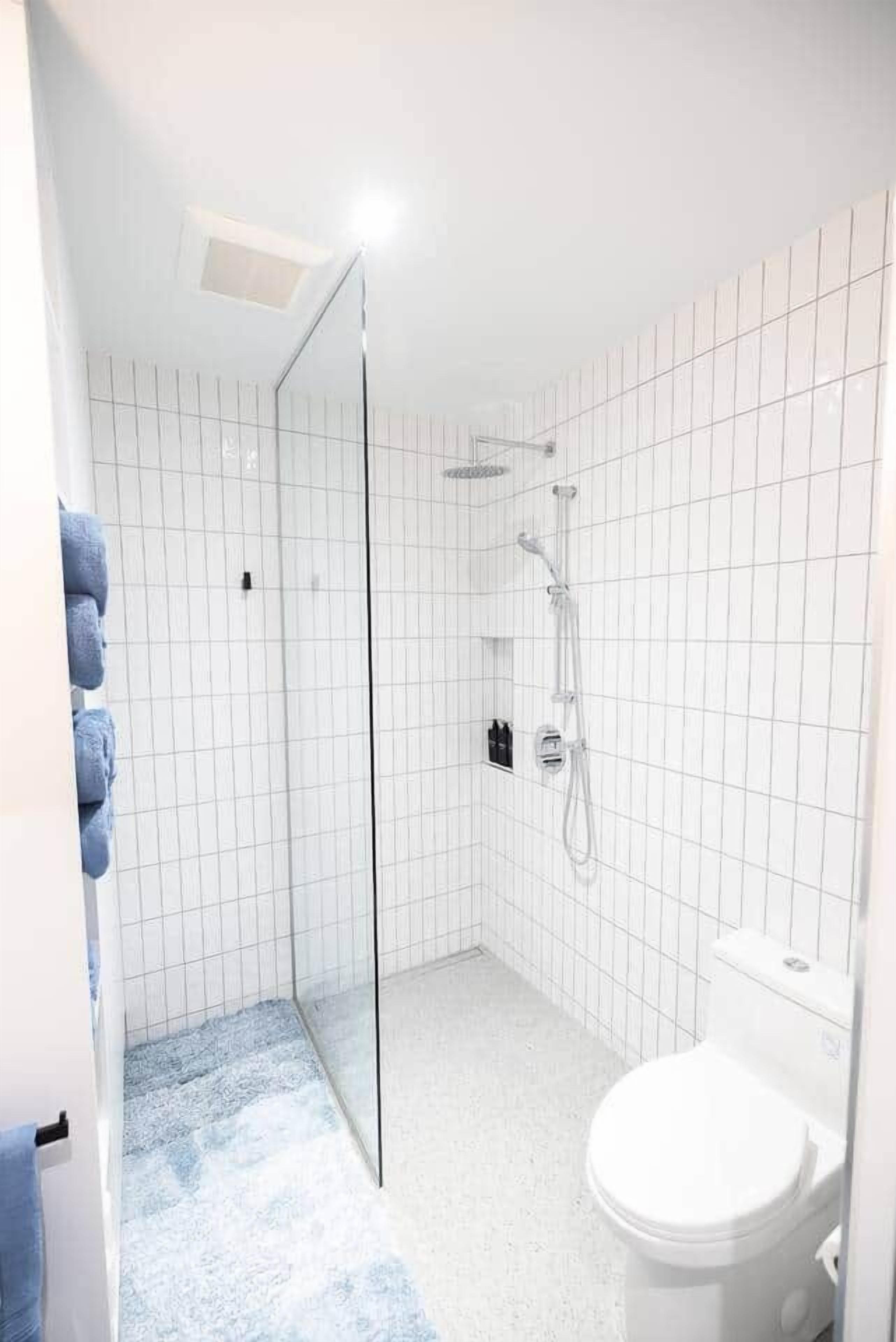 A bathroom with a glass shower enclosure, a toilet, and a tiled floor.