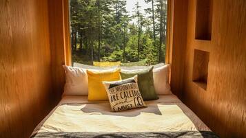 Acogedor cuarto tipo cabaña con asiento junto a la ventana, almohadones y vista a un bosque.