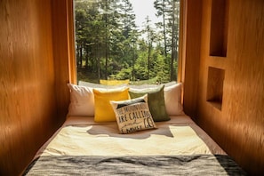 A cozy wooden cabin room with a window seat, pillows, and a view of a forest.