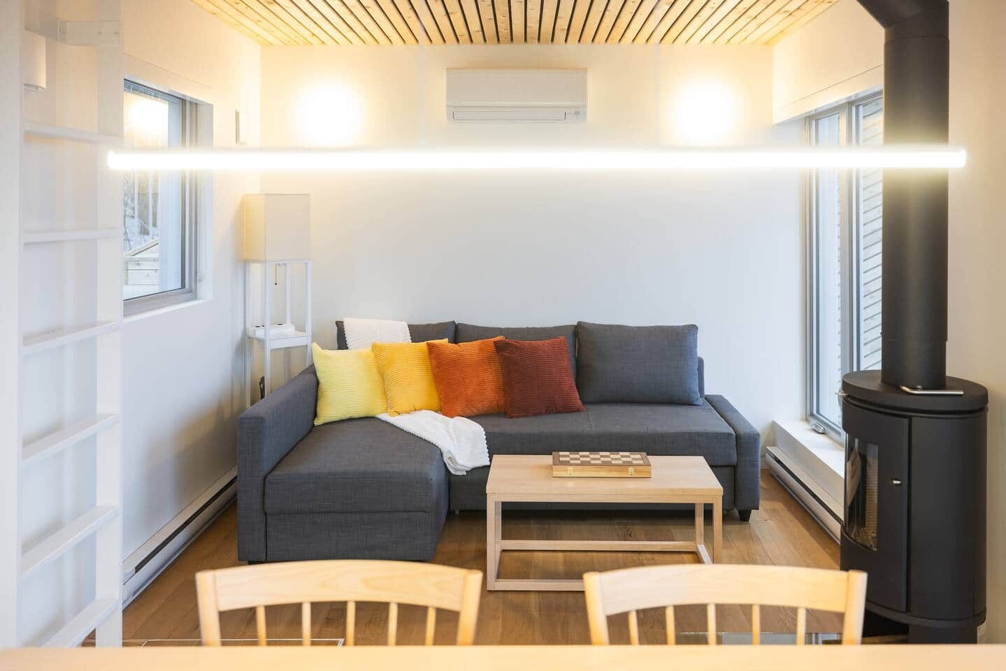 Un salon moderne avec un canapé, une table et une chaise. On y trouve une cheminée et une fenêtre avec des stores.
