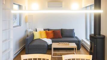Un salon moderne avec un canapé, une table et une chaise. On y trouve une cheminée et une fenêtre avec des stores.
