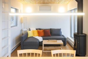 A modern living room with a sofa, a table, and a chair. There is a fireplace and a window with blinds.