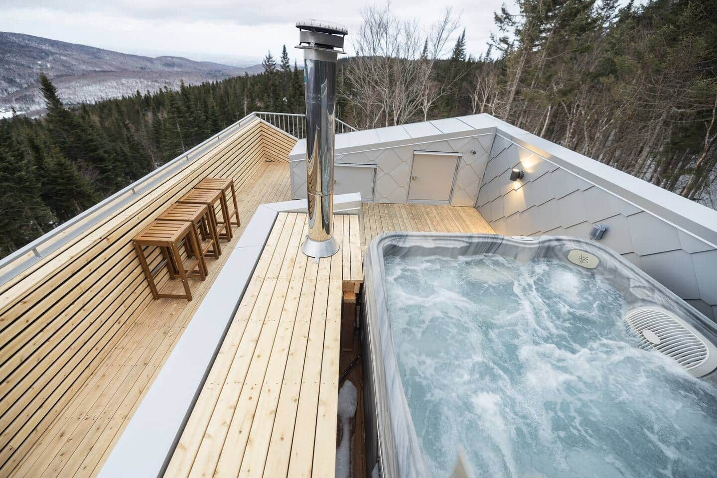 A hot tub on a wooden deck with a view of a forested mountain range.
