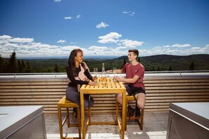 Zwei Personen sitzen an einem Holztisch auf einer Terrasse mit einem schönen Blick auf Berge und Bäume.