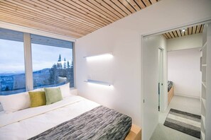 A modern bedroom with a large window, a bed, and a view of trees.