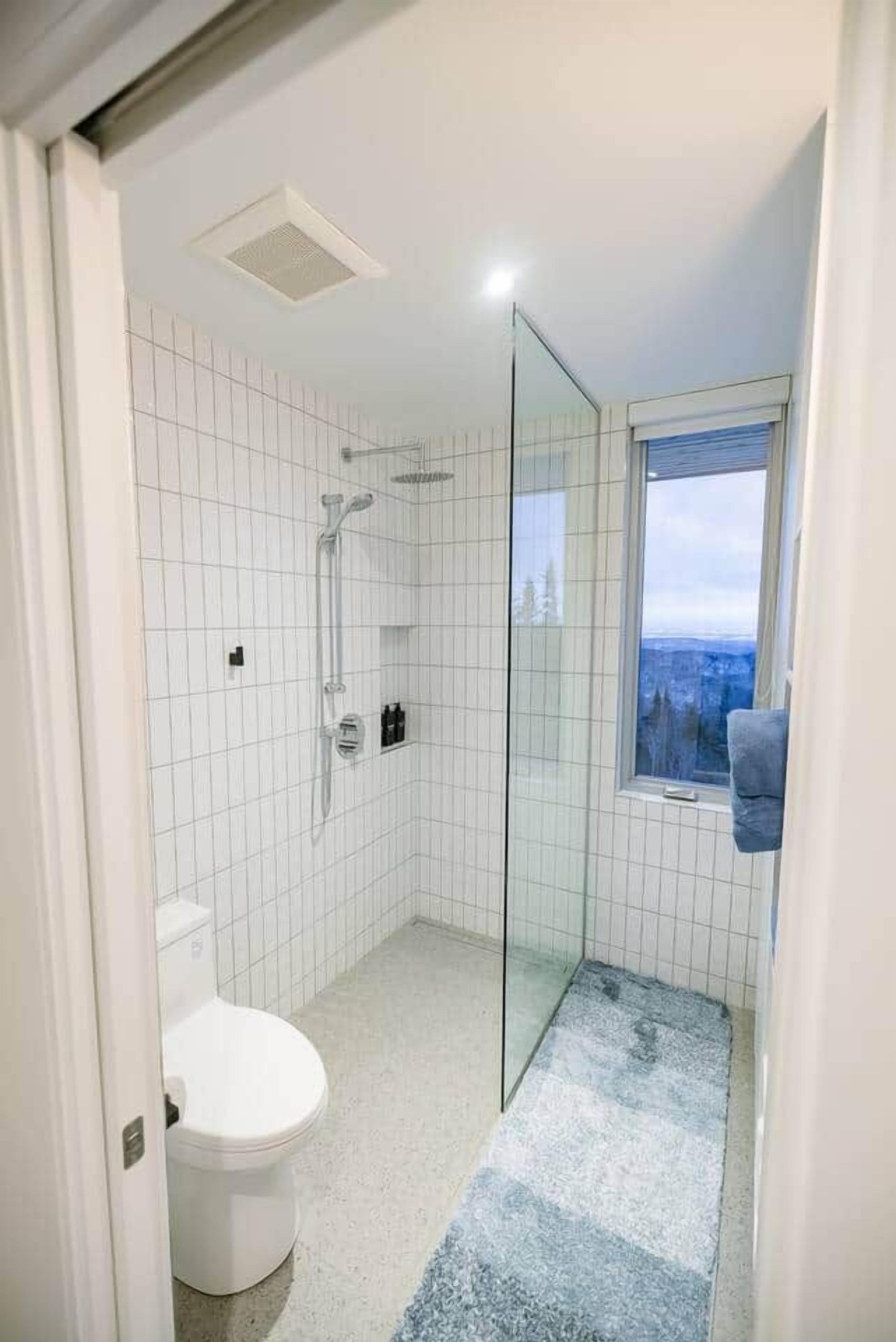 Moderni kylpyhuone, jossa on lasinen suihkuseinä, wc ja ikkuna, josta avautuu näkymä.