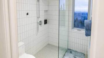 Moderni kylpyhuone, jossa on lasinen suihkuseinä, wc ja ikkuna, josta avautuu näkymä.