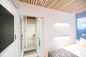 Ein modernes Schlafzimmer mit einem Bett, Nachttischen, einem großen Fenster und einer Tür zu einem anderen Raum.