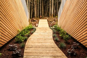 A wooden pathway flanked by vertical wooden panels, leading through a wooded area.