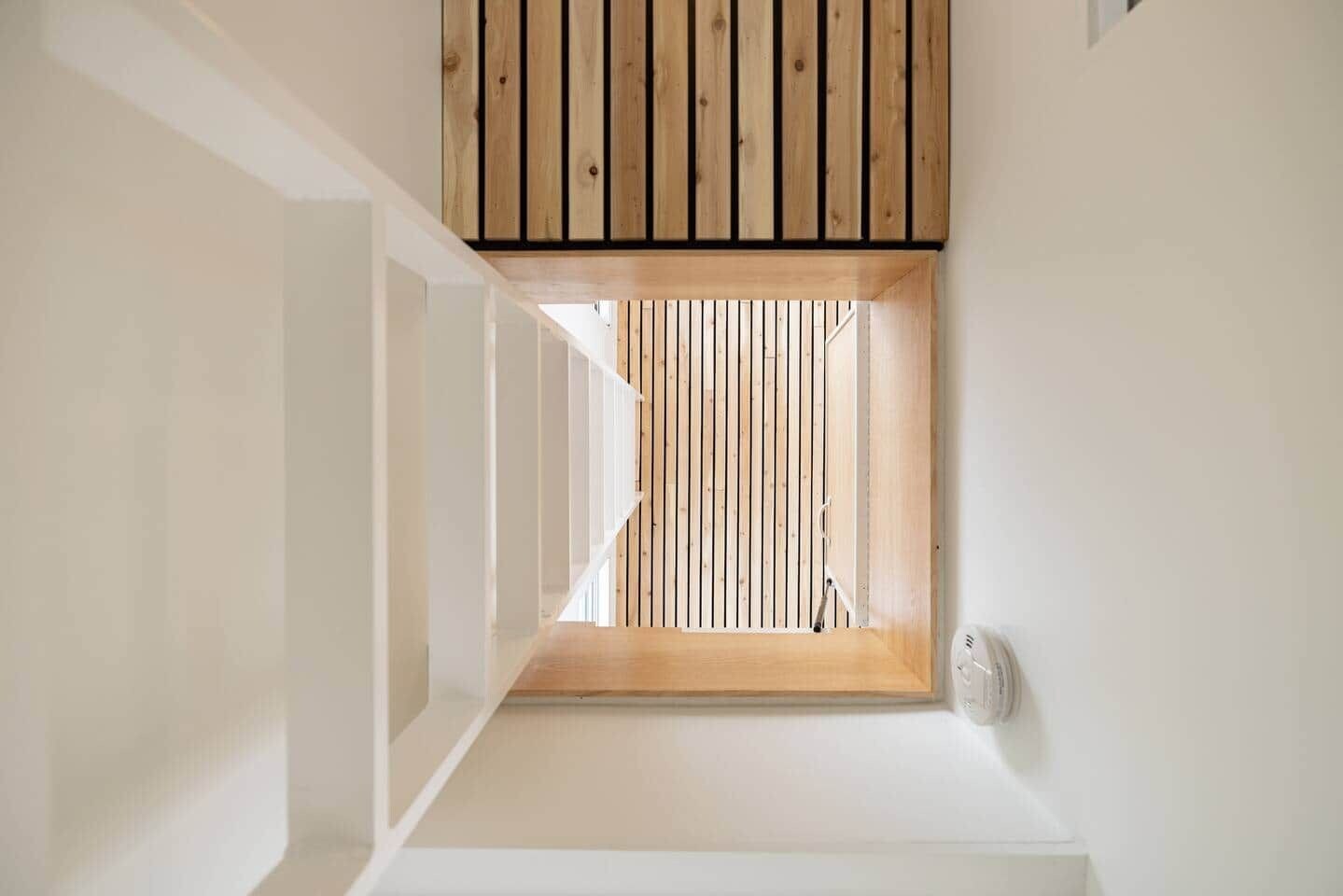Un couloir étroit avec une fenêtre à persiennes en bois et un mur blanc.