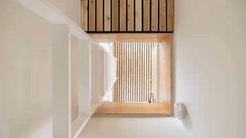 Un couloir étroit avec une fenêtre à persiennes en bois et un mur blanc.