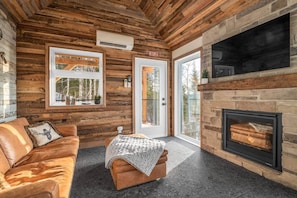 A cozy room with a leather sofa, a small ottoman, a fireplace, and large windows. - CHAMONIX / Micro-Chalet / Mountain Escape near Quebec City (Capitale-Nationale)