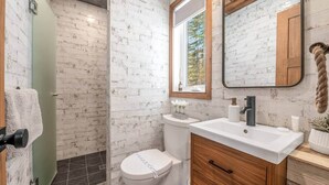 A bathroom with a white toilet, a wooden vanity, a mirror, and a shower area with a glass door. - CHAMONIX / Micro-Chalet / Mountain Escape near Quebec City (Capitale-Nationale)