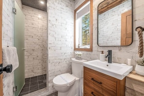 Ein Badezimmer mit einer weißen Toilette, einem Holzwaschtisch, einem Spiegel und einer Duschkabine mit Glastür.