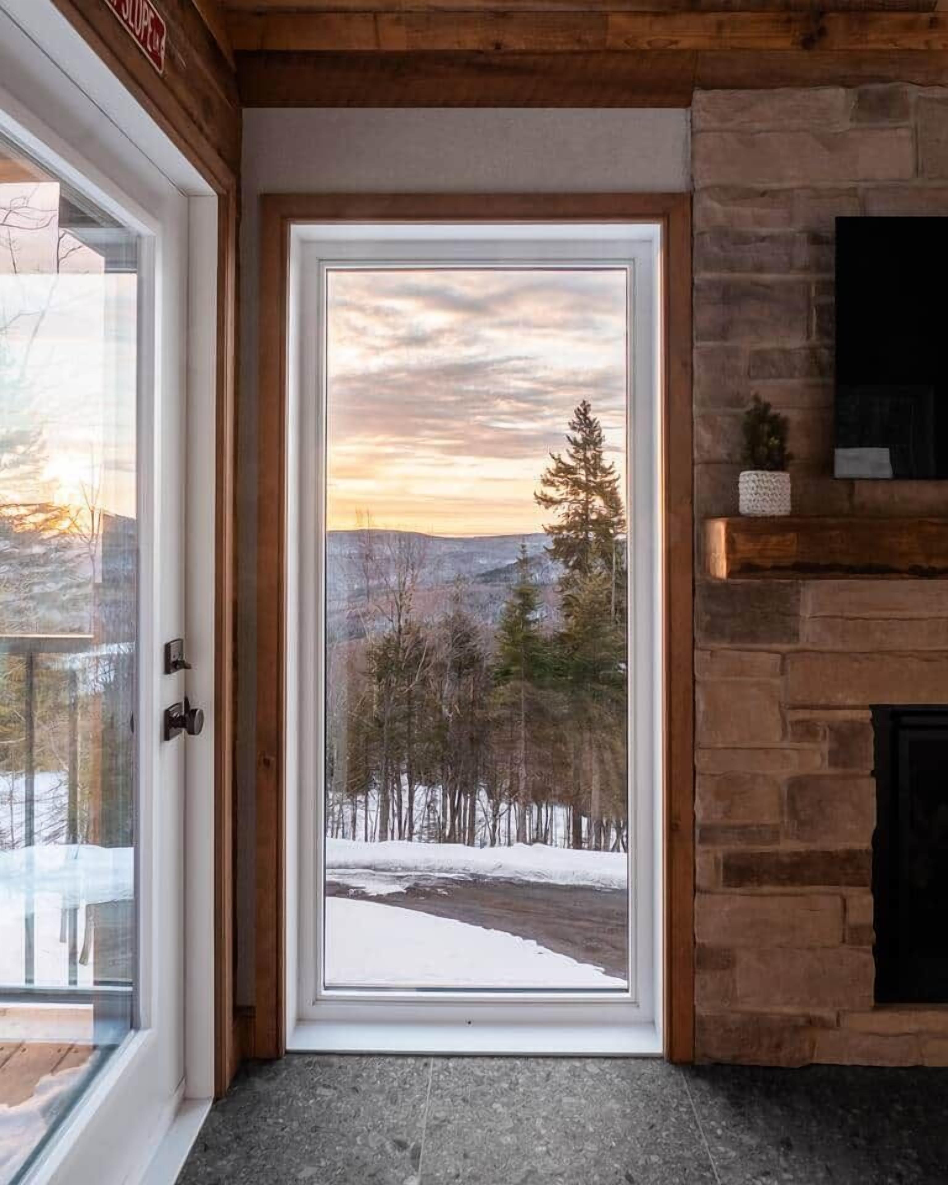 A door leading to a room with a stone fireplace and a view of a snowy landscape.
