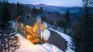 A wooden cabin with a balcony, surrounded by snow and trees, with a view of distant mountains. - CHAMONIX / Micro-Chalet / Mountain Escape near Quebec City (Capitale-Nationale)
