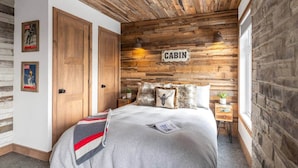 A cabin-themed bedroom with wooden walls, a bed with a grey blanket, and two doors. - CHAMONIX / Micro-Chalet / Mountain Escape near Quebec City (Capitale-Nationale)