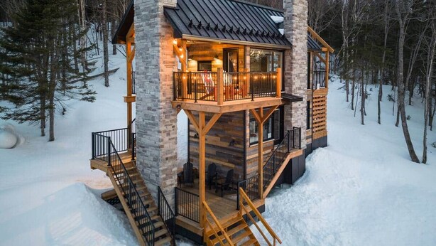 A two-story cabin with a stone exterior, wooden deck, and a staircase leading to the upper level. - CHAMONIX / Micro-Chalet / Mountain Escape near Quebec City (Capitale-Nationale)