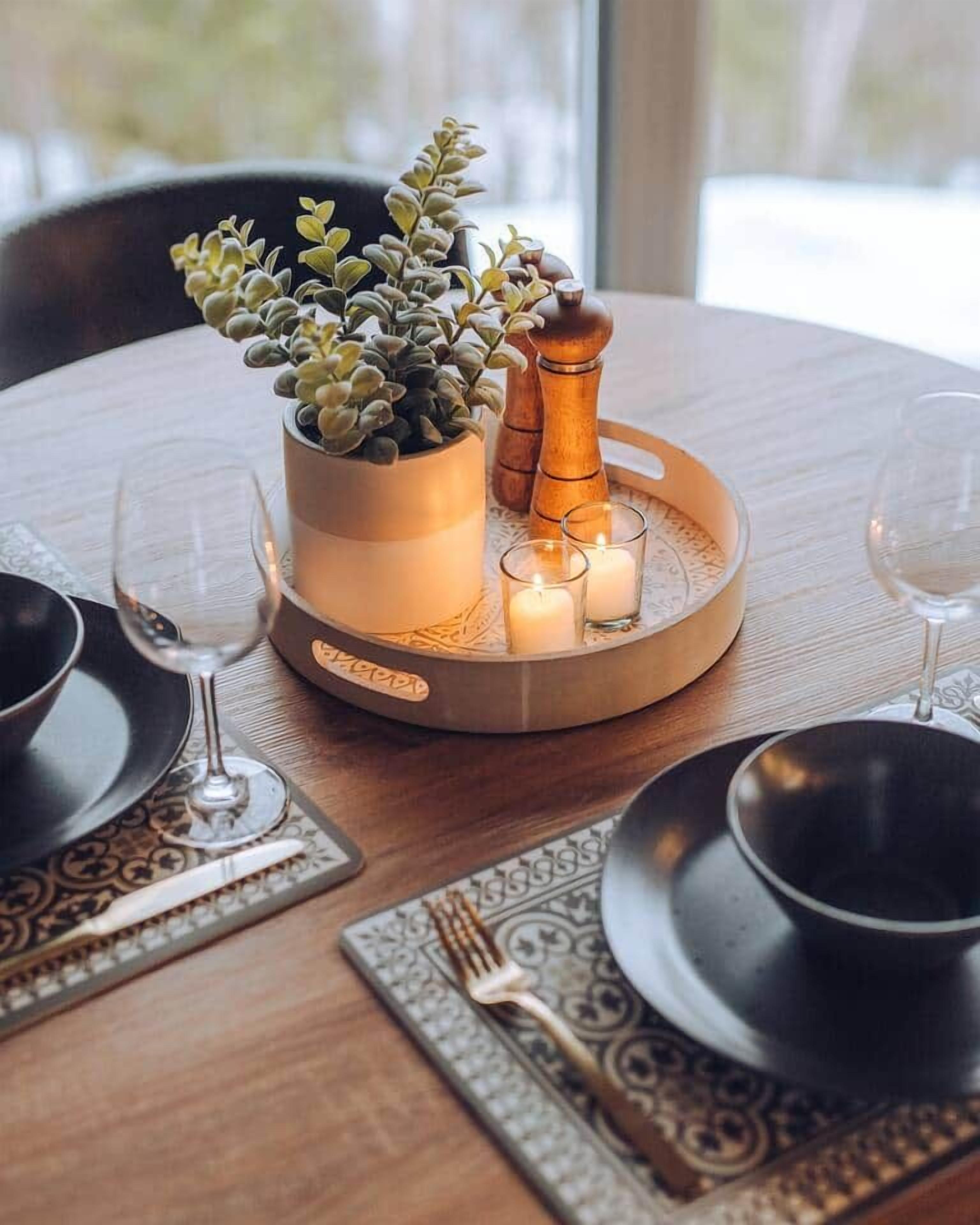 Una mesa de comedor dispuesta con una planta en maceta, velas y un molinillo de pimienta.