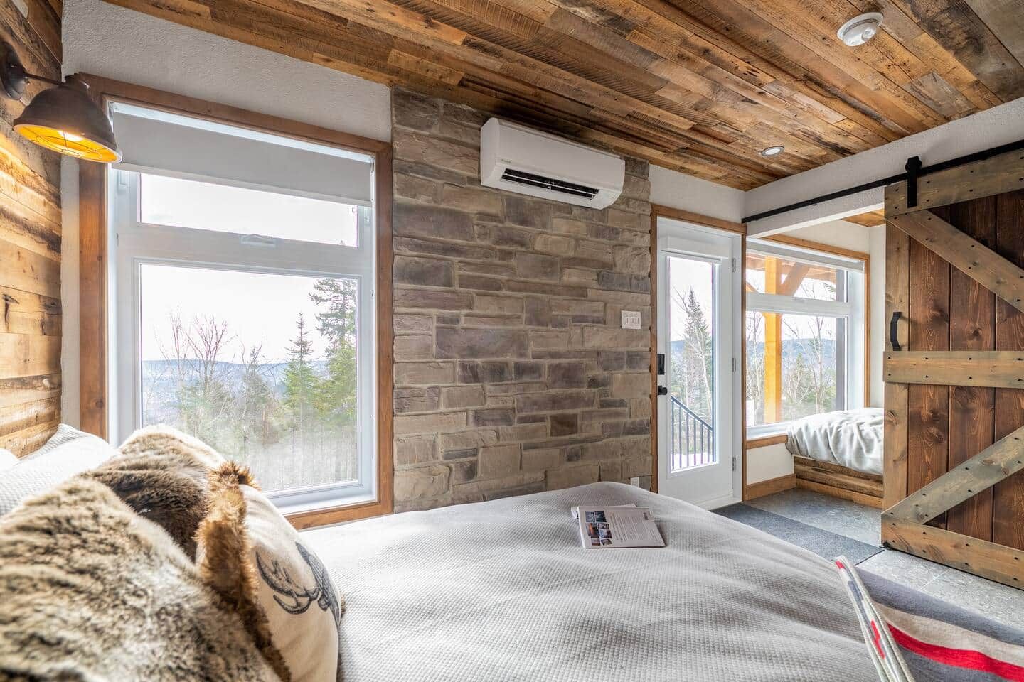 Une pièce avec un mur en pierre, de grandes fenêtres, un lit et une porte coulissante de style grange.