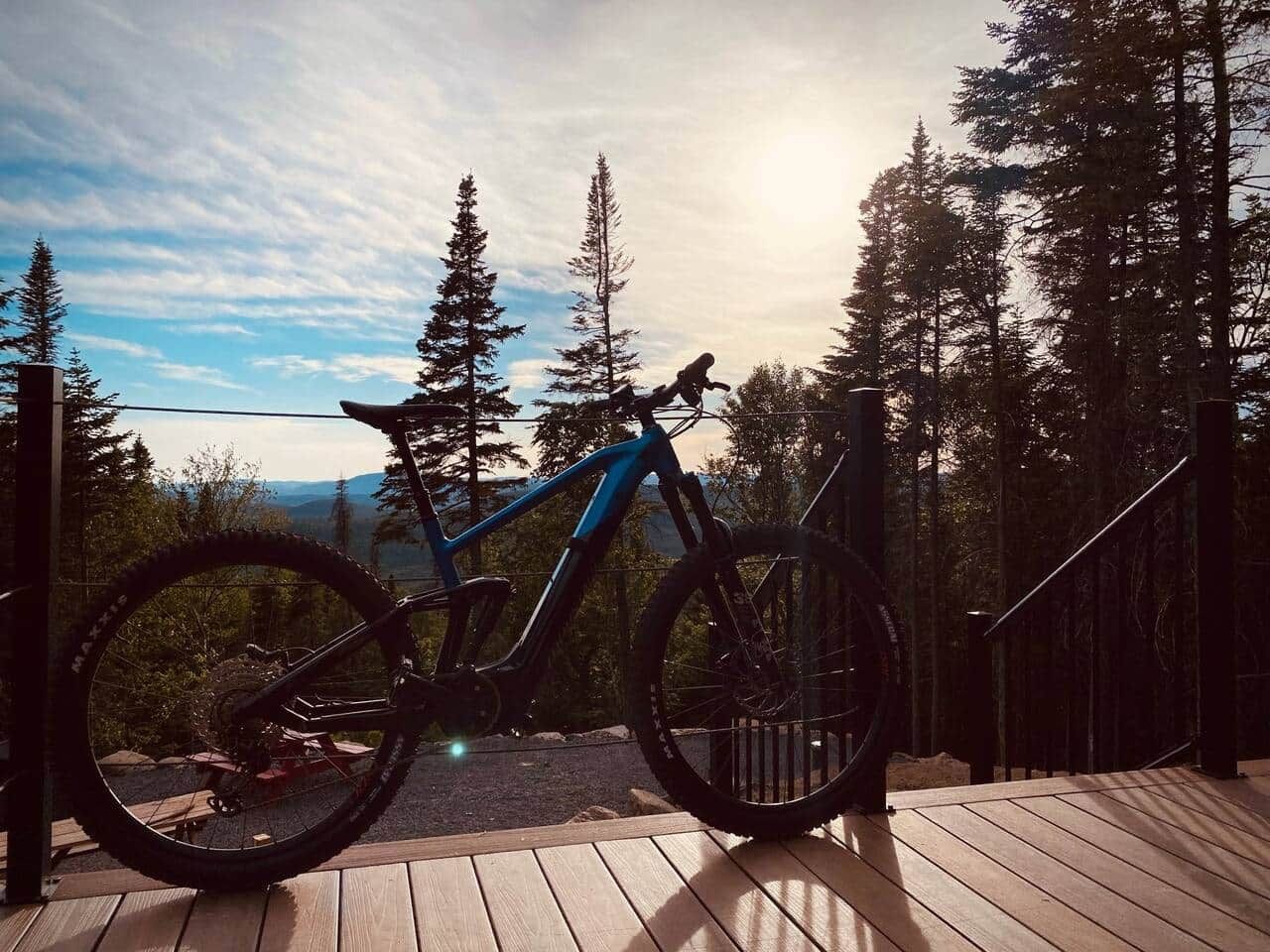 A mountain bike parked on a wooden deck with a view of a forest and mountains in the background.