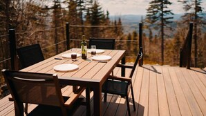 A wooden deck with a table set for two, surrounded by chairs, overlooking a forested landscape. - MIR / Micro-Chalet / Panoramic View (Capitale-Nationale)