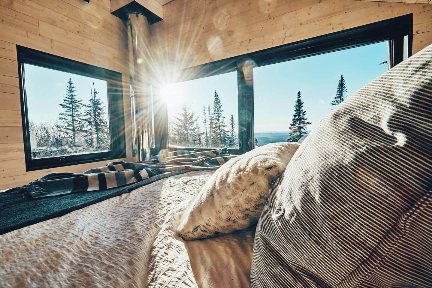 Una habitación acogedora con un ventanal grande, una cama con manta estampada y vistas a árboles.