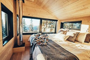 Interior de cabana com cama, janelas e lareira.
