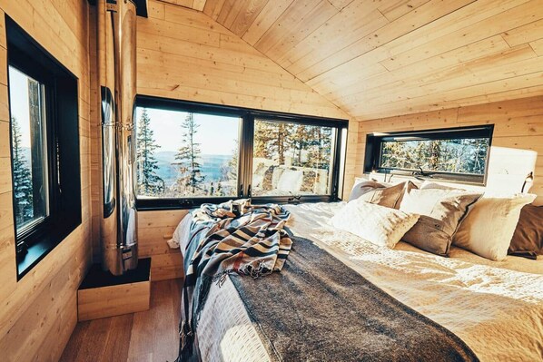 A cabin interior with a bed, windows, and a fireplace.
