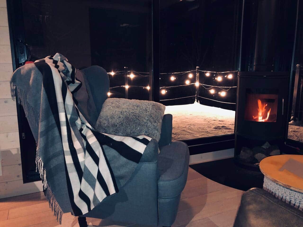 A cozy room with a fireplace, a chair with a blanket, and a view of the outdoors.