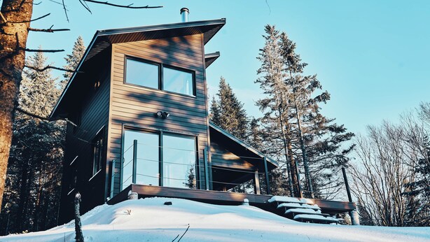 A modern two-story cabin with large windows, surrounded by snow-covered ground and tall trees. - MIR / Micro-Chalet / Panoramic View (Capitale-Nationale)