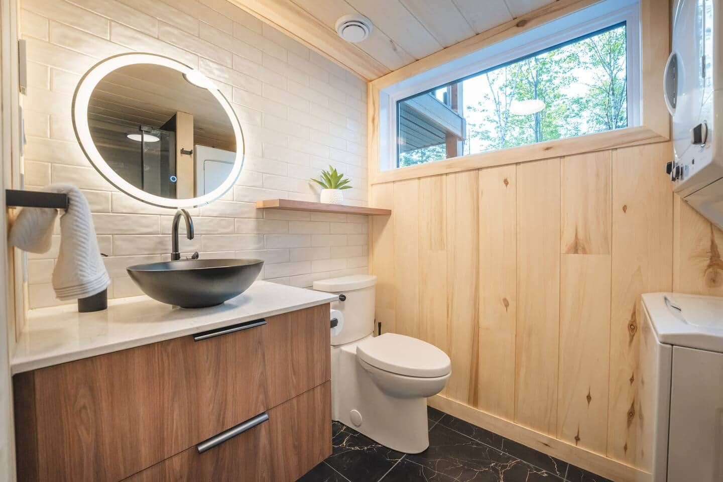 Un baño moderno con tocador de madera, espejo redondo, lavabo sobre encimera y un inodoro.